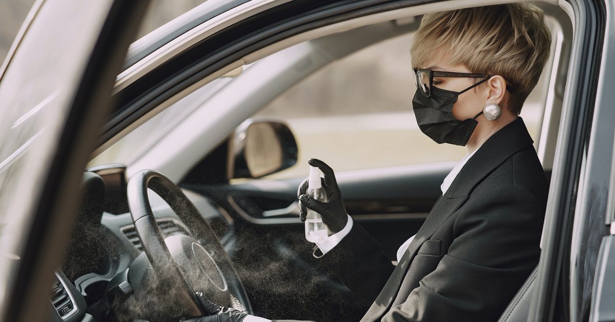 Mujer al volante, con mascarilla y desinfectando el auto.