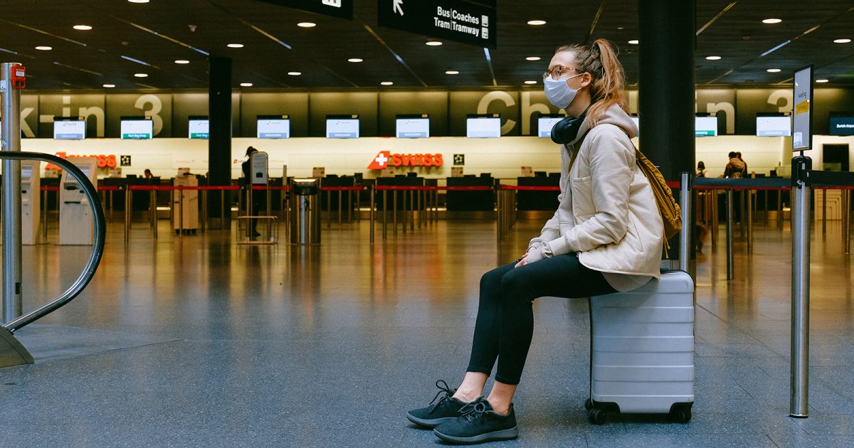 Viajera con mascarilla, sentada sobre su maleta en un aeropuerto