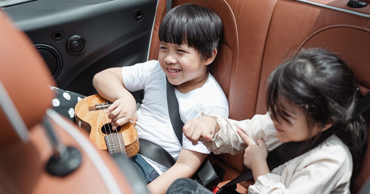Dos niños en el auto, con su cinturón de seguridad y jugando con un ukelele. Una demostración de que se puede conducir con niños, y que sea grato.