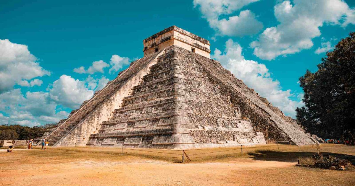 Foto de pirámide de México tomada desde abajo, visualizando toda la estructura con el fondo de cielo azulado y algunas nubes