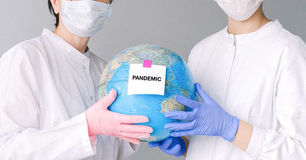 foto de dos personas sosteniendo un globo terraqueo que tiene un cartel que dice pandemia