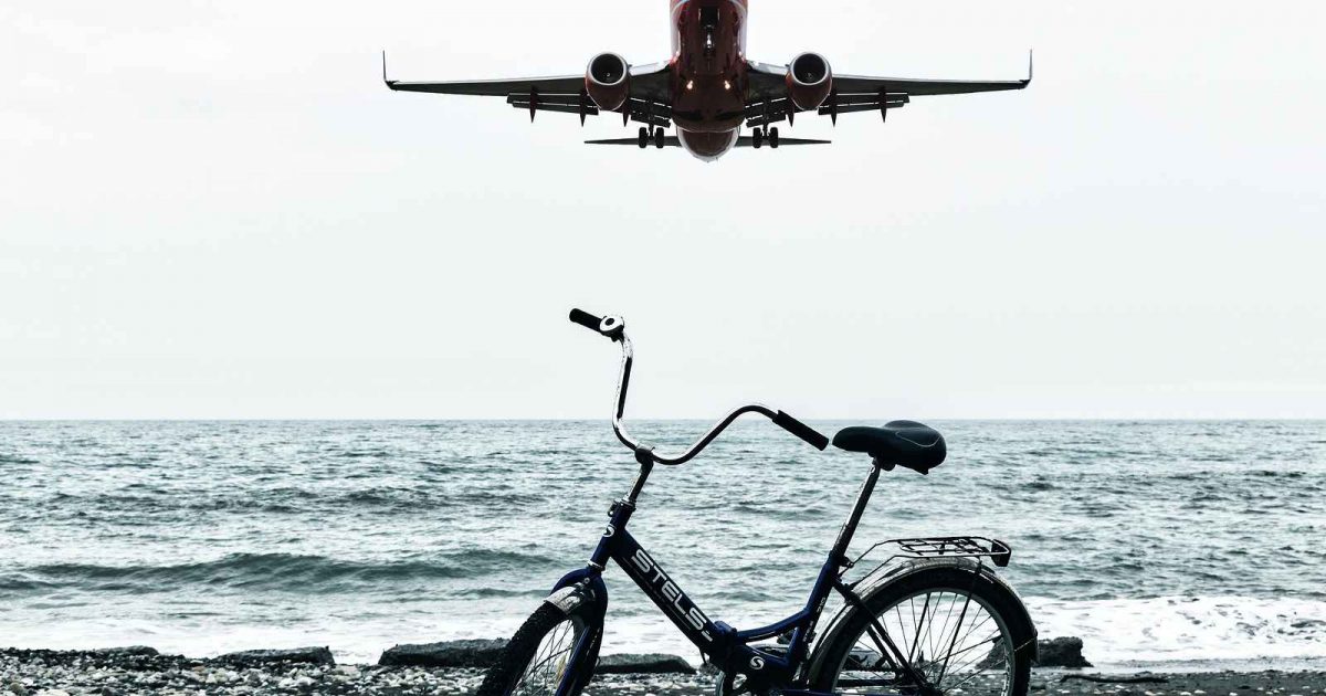 foto de una bicicleta con un avión volando por encima de ésta misma en la playa